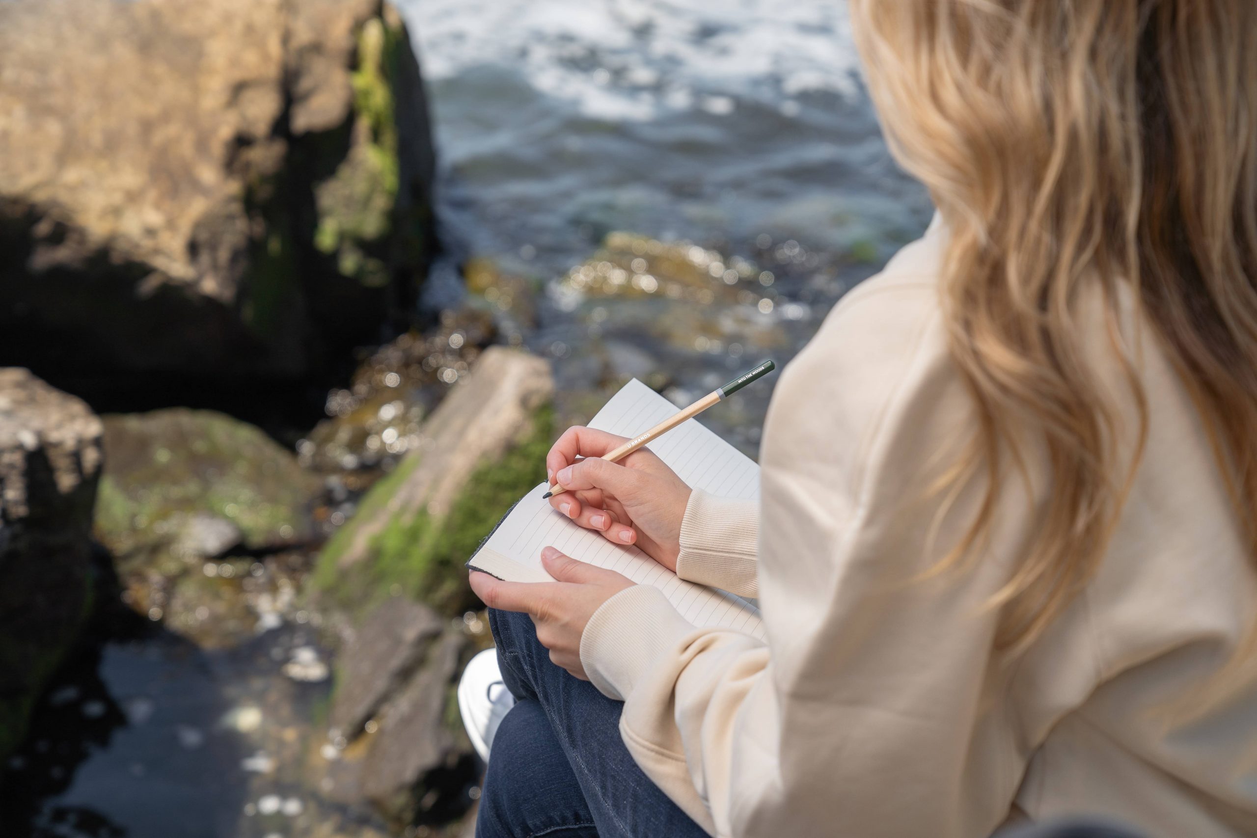 woman sitting on a rock by the water writing in her journal